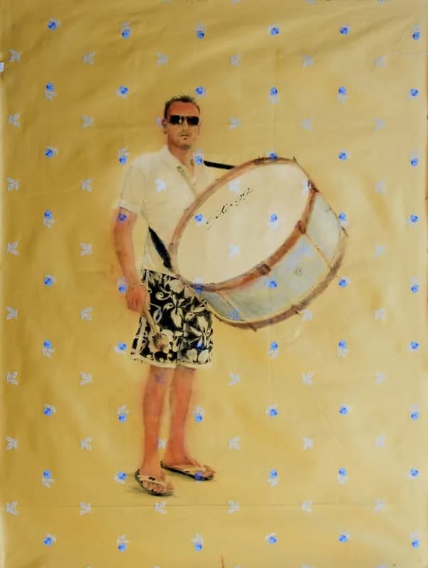 Uomo con occhiali da sole, polo bianca, pantaloncini neri e infradito, in piedi accanto a un grande tamburo sospeso in diagonale, su un fondo giallo decorato da piccoli fiori azzurri.