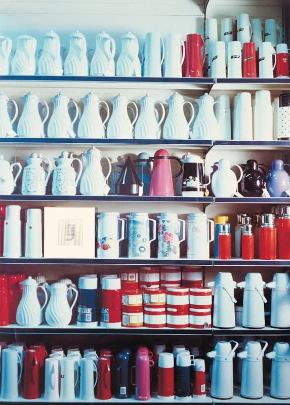 Scaffale metallico a sette ripiani colmo di brocche, thermos e contenitori, soprattutto bianchi con dettagli rossi, azzurri, neri e rosa.
